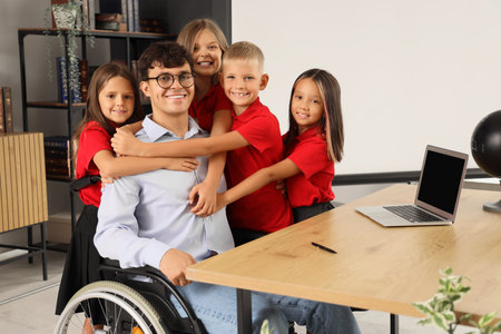 Male teacher in wheelchair with little pupils hugging at schoolの写真素材