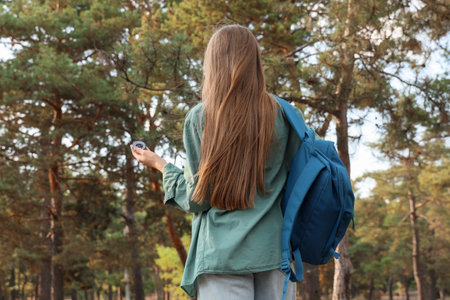 Female traveler with compass and backpack in forest, back viewの写真素材