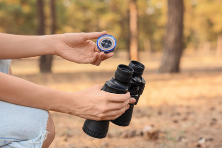 Female traveler with compass and binoculars in forest, closeup