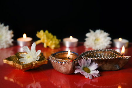 Diya lamps with beautiful flowers and burning candles on color background. Divaly celebration