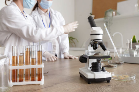 Microscope with test tubes and Petri dishes on table in laboratory, closeup