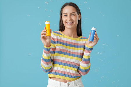 Young woman holding bottles with soap bubbles on blue background