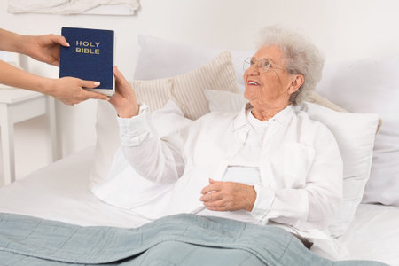 Caregiver giving Bible to senior woman at home