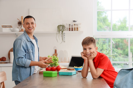 Happy father packing school lunchbox for his little son in kitchenの写真素材