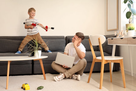 Naughty little boy playing with toy gun and his working father at home