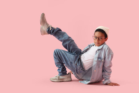 Little African-American boy in adult clothes on pink background