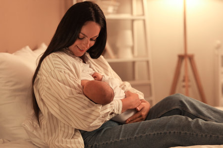 Mother breastfeeding her baby in bedroom at nightの写真素材