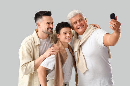 Teenage boy with his dad and grandfather taking selfie on light backgroundの写真素材