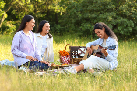 Female friends playing guitar on picnic in parkの写真素材