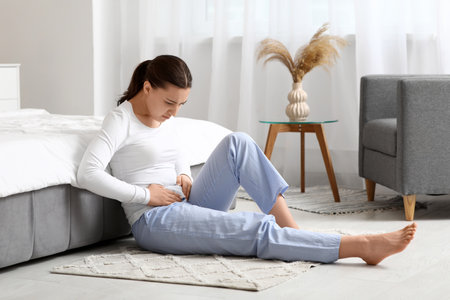 Young woman suffering from cystitis in bedroomの写真素材
