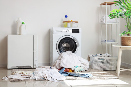 Interior of light laundry room with modern washing machine and pile of dirty clothes on floorの写真素材
