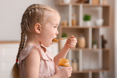 Cute little girl with spoon eating jam at homeの写真素材