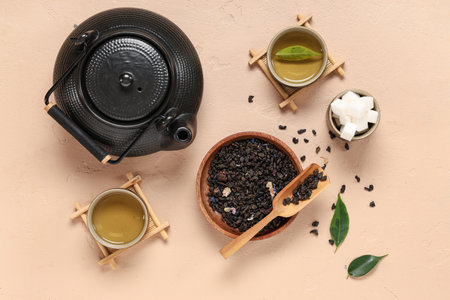 Teapot with cups, wooden bowl of dry tea and sugar on beige backgroundの写真素材