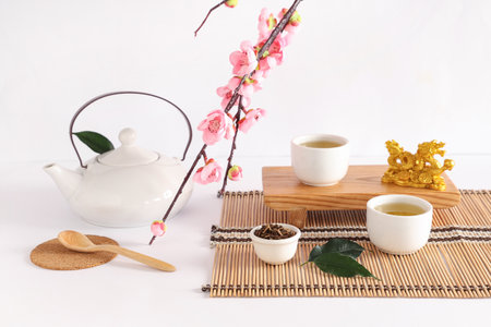 Wooden stand with teapot, cups, dry tea and sakura branch on white backgroundの写真素材