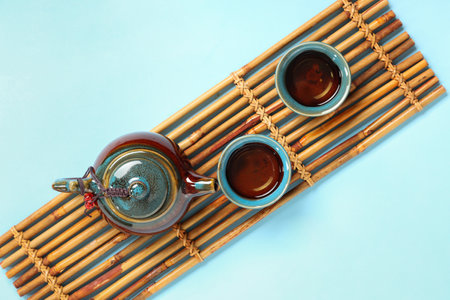 Bamboo mat with teapot and cups of tea on blue backgroundの写真素材