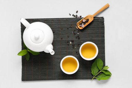 Teapot with cups, wooden scoop of dry tea and leaves on white backgroundの写真素材