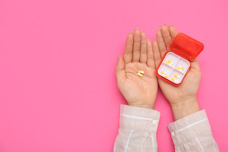 Female hands with pills in case on pink backgroundの写真素材