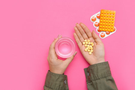 Female hands with pills and glass of water on pink backgroundの写真素材