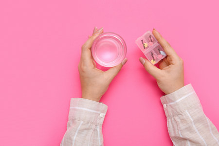 Female hands with pills in case and glass of water on pink backgroundの写真素材