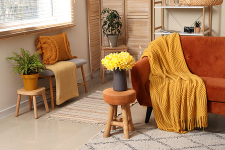 Comfortable sofa with plaid and beautiful daffodils in living room