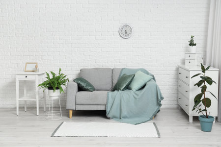 Gray sofa, houseplants, chest of drawers and clock on white brick wall in stylish living roomの写真素材