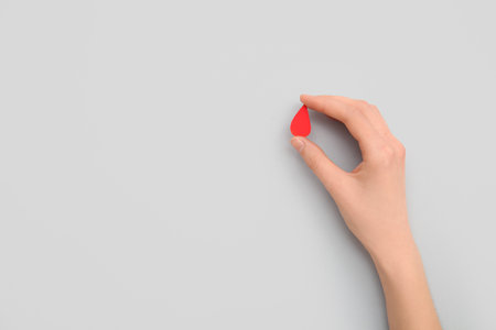 Female hand with paper blood drop on gray background. Donation blood concept.の写真素材