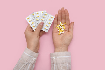 Female hands with pills in blister packs on pink backgroundの写真素材