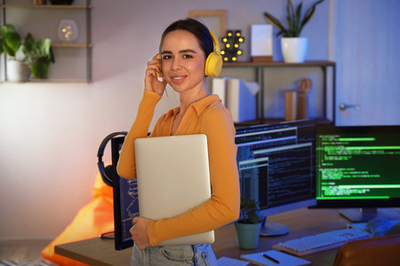 Female programmer with headphones and laptop in office at night