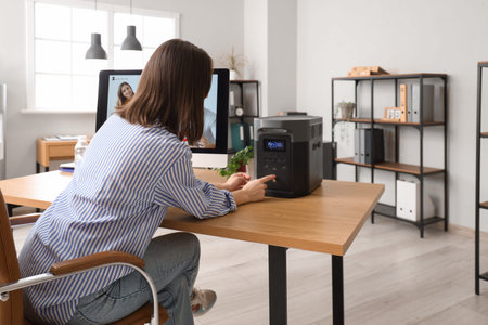 Young woman turning portable solar station on desk in office, back view