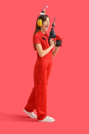Happy female worker in Santa hat with gift drill on red backgroundの写真素材