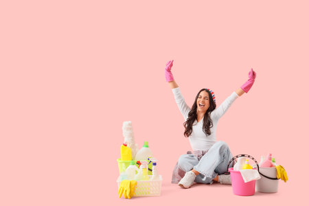 Happy housewife with cleaning supplies sitting on pink backgroundの写真素材