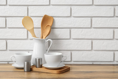 Porcelain cups and wooden utensils on table near white brick wallの写真素材