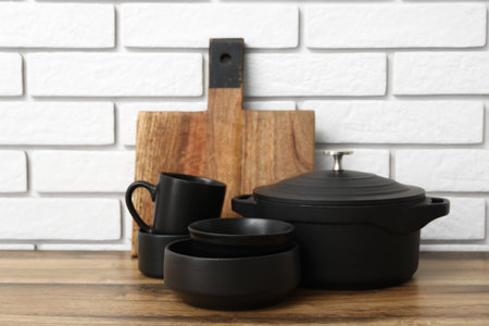 Black bowls, cups and cooking pot on wooden table near white brick wallの写真素材