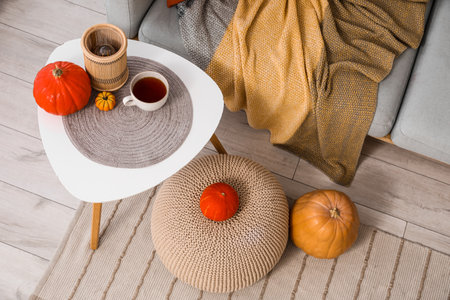 Coffee table with cup of tea, pouf and pumpkins in interior of living roomの写真素材