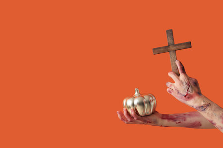 Zombie hands with wooden cross and pumpkin on orange background. Halloween celebrationの写真素材