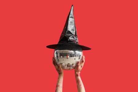 Zombie hands holding disco ball with witch hat on red background. Halloween celebrationの写真素材