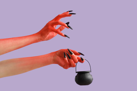 Devil hands with cauldron on lilac background. Halloween celebrationの写真素材