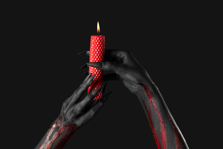 Bloody witch hands with claws and burning wax candle on black background. Halloween celebrationの写真素材