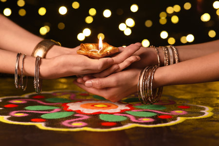 Female hands with diya lamp for Diwali on dark blurred backgroundの写真素材
