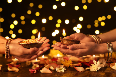 Women holding beautiful diya lamps for Diwali with candles, flowers and petals on dark blurred backgroundの写真素材