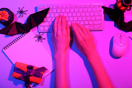 Female hands with computer keyboard, mouse, notebook and decorations for Halloween on color background, closeupの写真素材