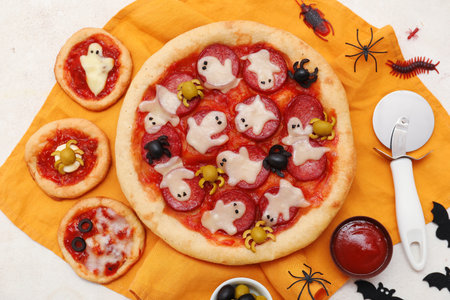 Composition with tasty pizzas, cutter and decorations for Halloween on light backgroundの写真素材