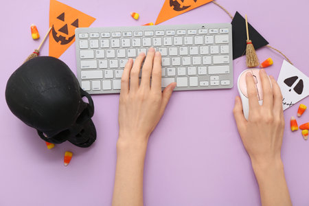 Female hands with computer keyboard, mouse and decorations for Halloween on lilac background, closeupの写真素材