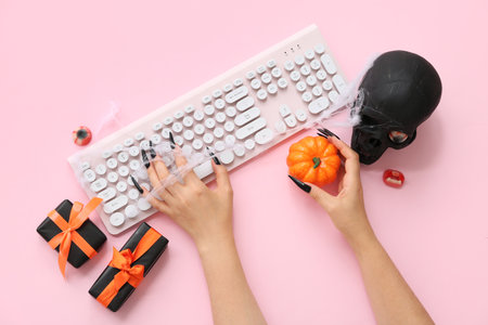 Witch's hands with computer keyboard, gifts and decorations for Halloween on pink background, closeupの写真素材