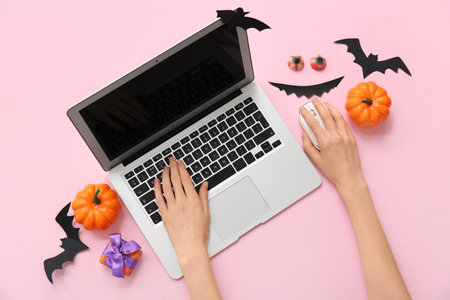 Female hands with modern laptop, decorations and gift box for Halloween on pink backgroundの写真素材