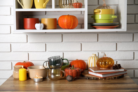 Dishware with pumpkins, books and burning candles on counter near white brick wallの写真素材