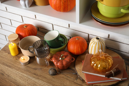 Dishware with pumpkins, books and burning candles on counter near white brick wallの写真素材