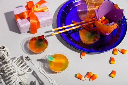 Tasty jelly dessert, candy corns, tableware and gift for Halloween on gray backgroundの写真素材