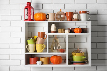Shelves with dishware and pumpkins on white brick wallの写真素材