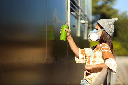 Young woman in respirator with spray can painting graffiti on wall outdoorsの写真素材